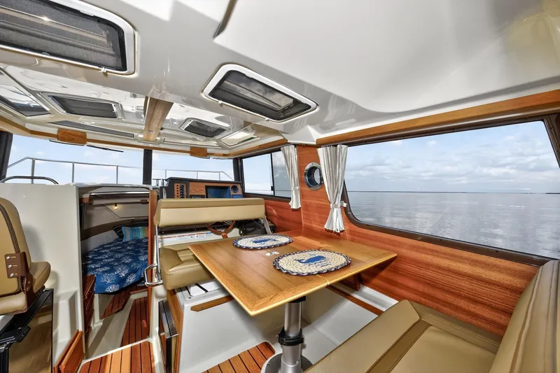 Slide: The Image of 2024 Ranger Tugs R-27 interior with dining area, wood accents, and ocean view. - 31