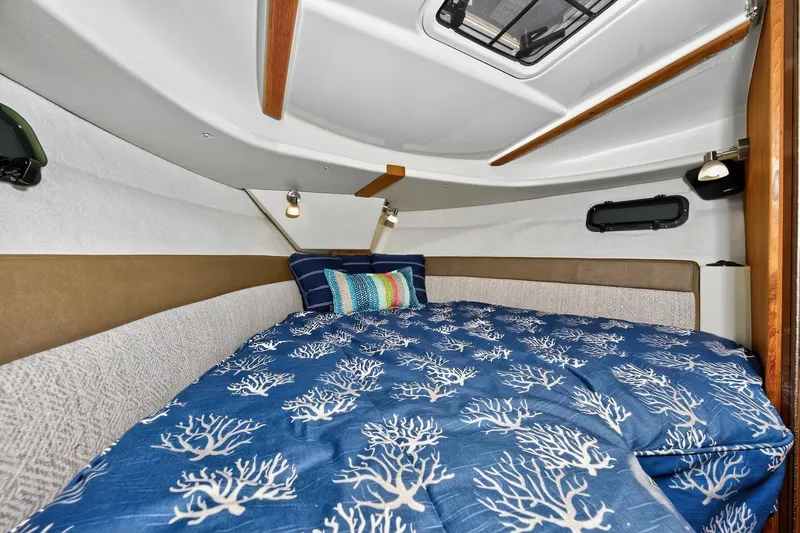 Slide: The Image of 2024 Ranger Tugs R-27 cabin interior with cozy bed and nautical-themed bedding. - 46