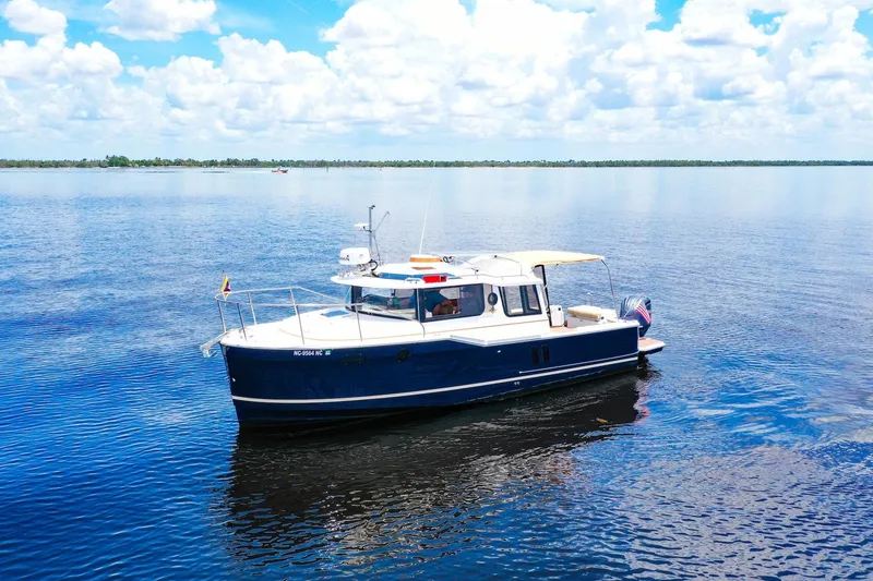 Slide: The Image of 2024 Ranger Tugs R-27 boat cruising on a calm lake under a blue sky. - 6