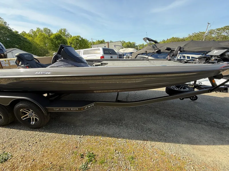 Slide: The Image of 2025 Skeeter ZXR21 boat on trailer, parked outdoors, under clear blue sky. - 19