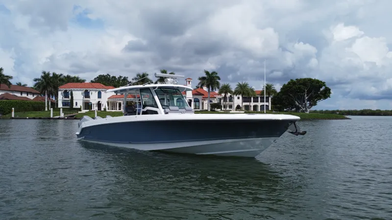 Slide: The Image of 2027 Boston Whaler 380 Outrage on calm water, in front of a villa with palm trees. - 0
