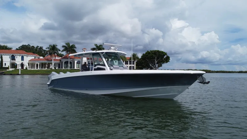 Slide: The Image of A 2027 Boston Whaler 380 Outrage on the water in front of a villa with palm trees. - 2