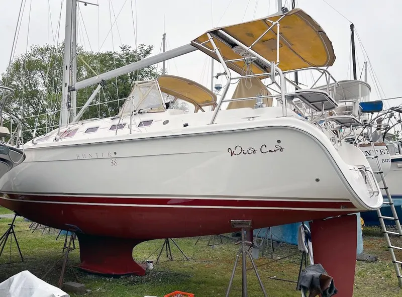The Image of 2005 Hunter 38 sailboat on stands, named "Wild Card," with red hull and yellow canopy. - 0