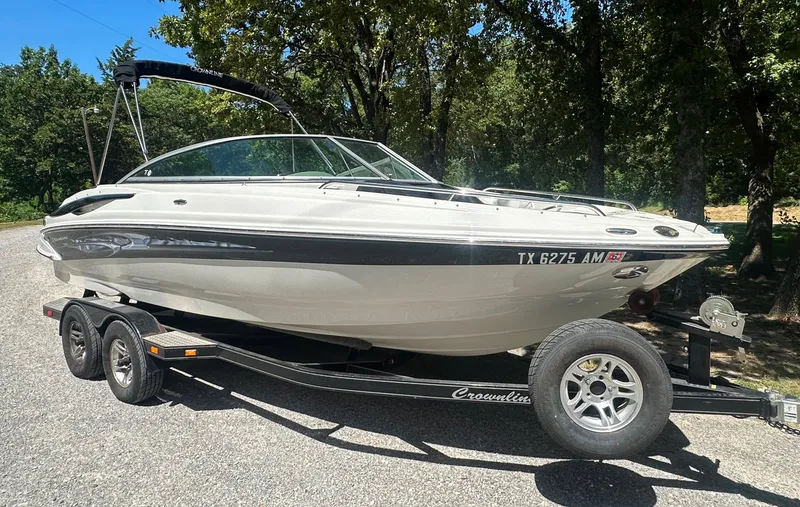 Slide: The Image of 2007 Crownline 220 LS boat on trailer, parked outdoors, surrounded by trees. - 2
