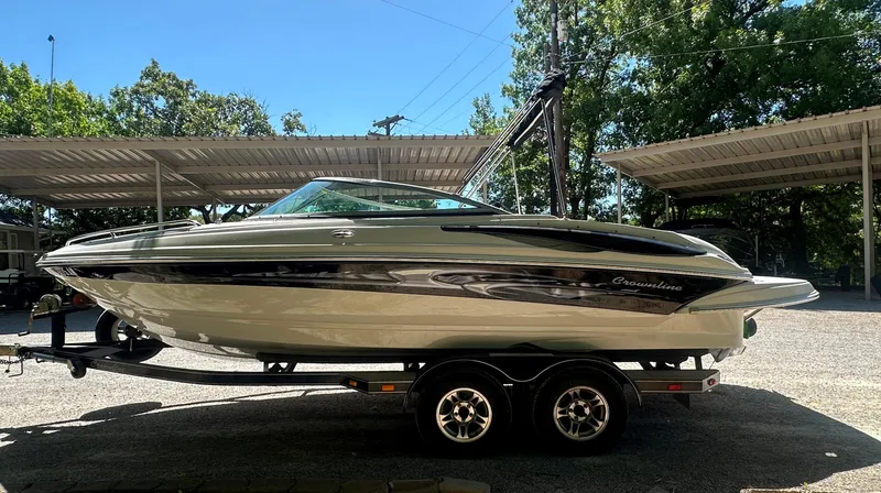 Slide: The Image of 2007 Crownline 220 LS boat on trailer, parked under a metal canopy, surrounded by trees. - 5