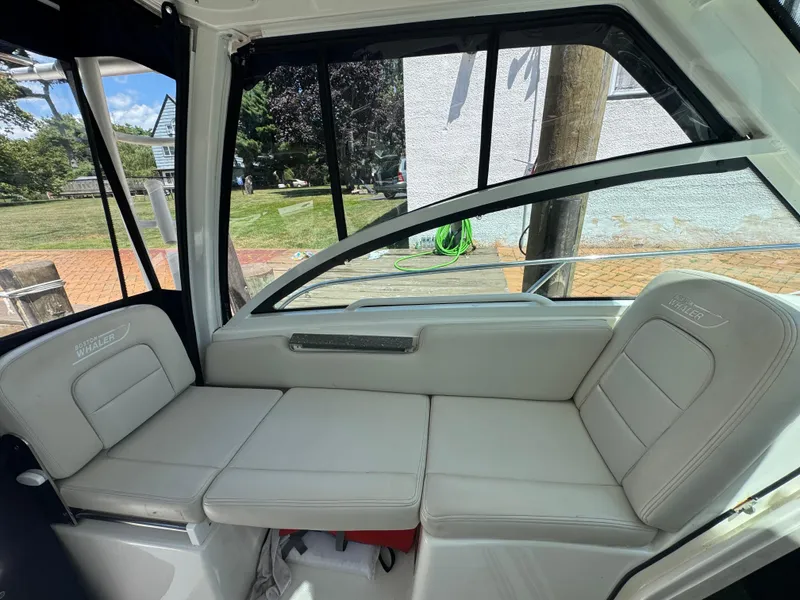 Slide: The Image of 2019 Boston Whaler 285 Conquest interior seating with white cushions and window view. - 33