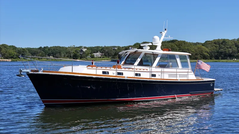 Slide: The Image of 2002 Grand Banks 49 Eastbay HX yacht on calm water, with American flag, under clear blue sky. - 7