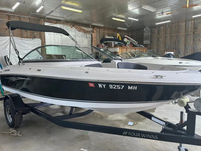 Slide: The Image of 2011 Four Winns H180 boat in a garage, black and white exterior, on a trailer. - 11
