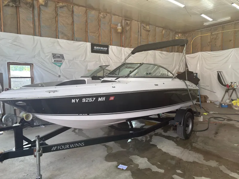 Slide: The Image of 2011 Four Winns H180 boat in garage, black and white exterior, on trailer. - 16
