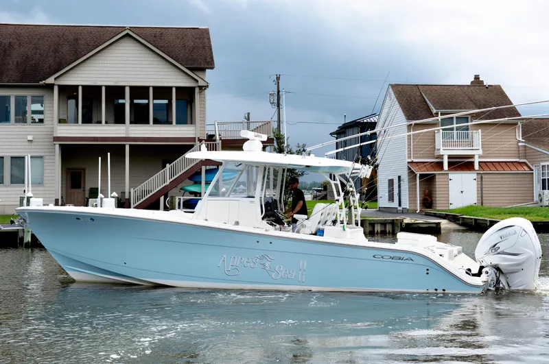 Slide: The Image of 2024 Cobia 350 boat cruising near waterfront homes under cloudy skies. - 3