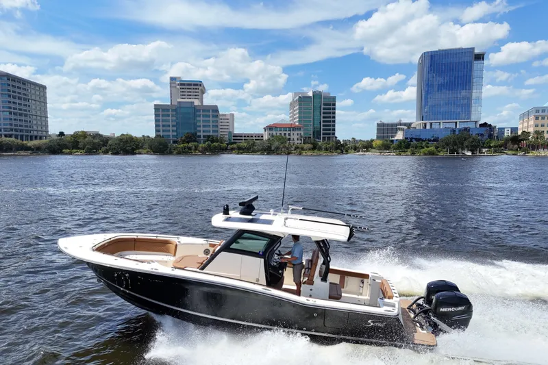 Slide: The Image of 2021 Scout 330 LXF boat cruising on a river with city skyline backdrop. - 101