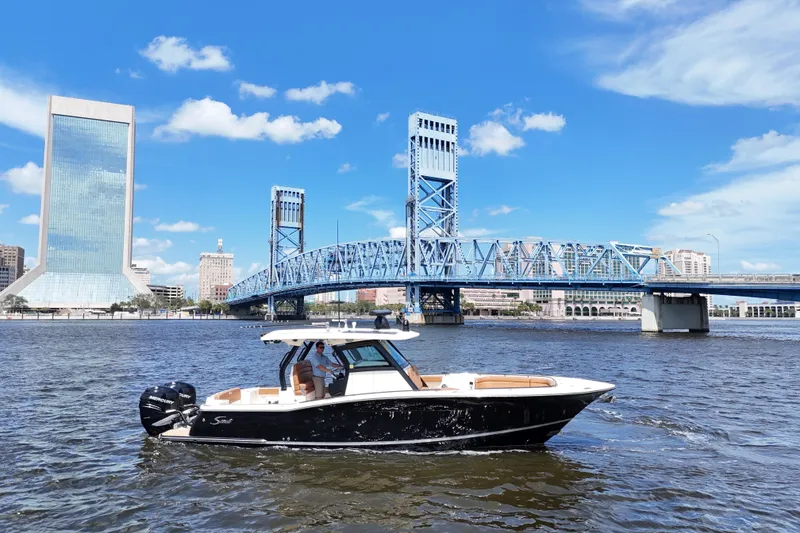 Slide: The Image of 2021 Scout 330 LXF boat cruising near a blue bridge and city skyline. - 11