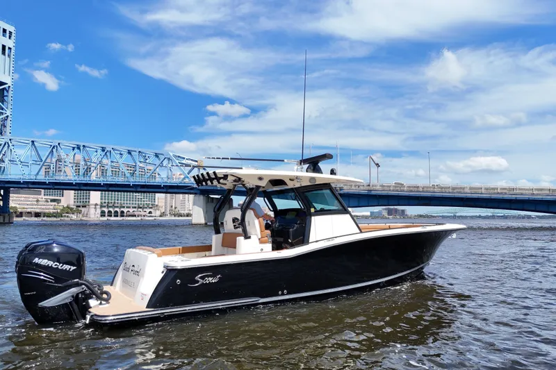 Slide: The Image of 2021 Scout 330 LXF boat on water near a blue bridge under a clear sky. - 12