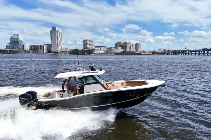 Slide: The Image of 2021 Scout 330 LXF boat cruising on a river with city skyline backdrop. - 13
