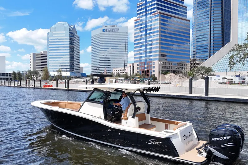 Slide: The Image of 2021 Scout 330 LXF boat cruising near city skyscrapers on a sunny day. - 14