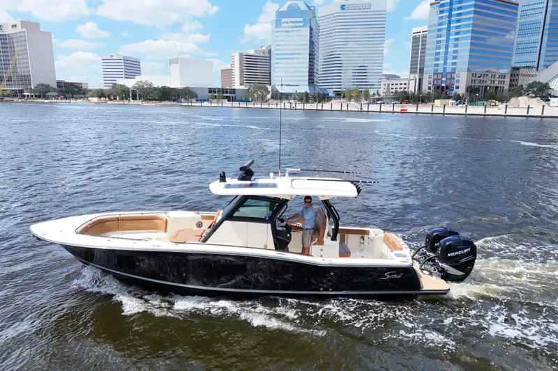 Slide: The Image of 2021 Scout 330 LXF boat cruising on a river with city skyline backdrop. - 15