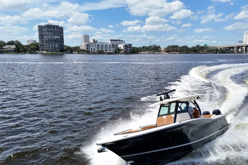 Slide: The Image of 2021 Scout 330 LXF boat cruising on a river with cityscape background. - 16
