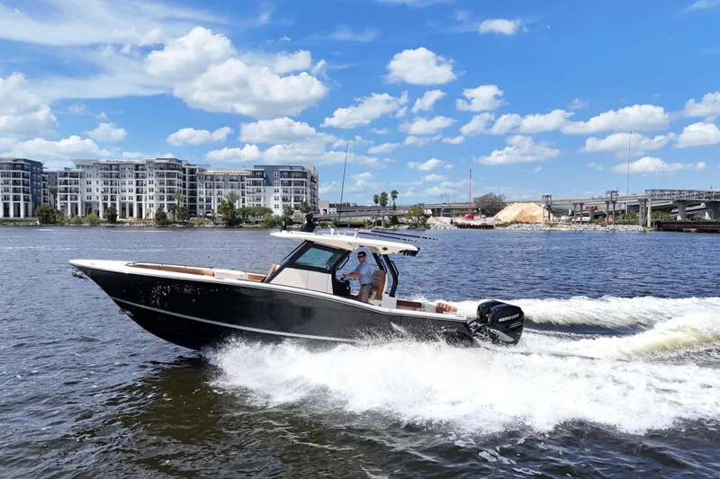 Slide: The Image of 2021 Scout 330 LXF boat cruising on a river with cityscape background. - 19
