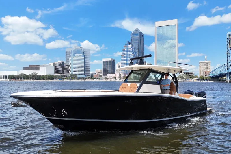 Slide: The Image of 2021 Scout 330 LXF boat cruising on a river with city skyline backdrop. - 2