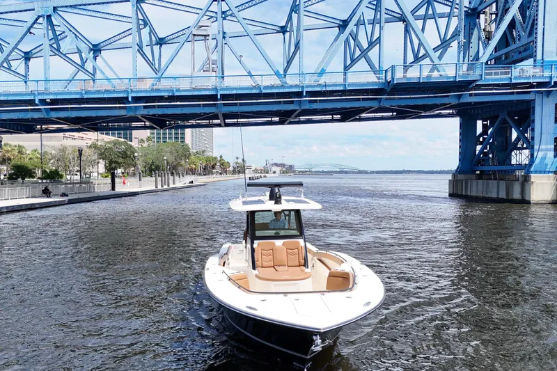 Slide: The Image of 2021 Scout 330 LXF boat cruising under a blue bridge on a sunny day. - 20