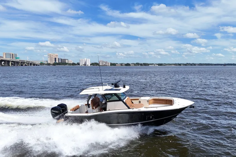 Slide: The Image of 2021 Scout 330 LXF boat cruising on a sunny day with cityscape background. - 22