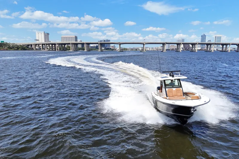Slide: The Image of 2021 Scout 330 LXF boat cruising on a river with city skyline backdrop. - 24