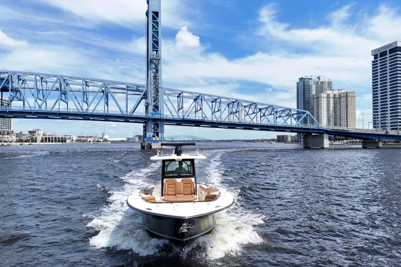 Slide: The Image of 2021 Scout 330 LXF boat cruising under a blue bridge in an urban waterfront setting. - 25