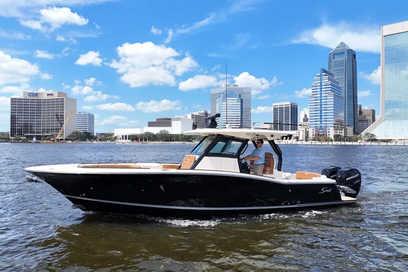Slide: The Image of 2021 Scout 330 LXF boat cruising on a river with city skyline backdrop. - 3
