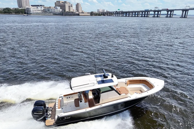 Slide: The Image of 2021 Scout 330 LXF boat cruising on a river with cityscape and bridge in background. - 30