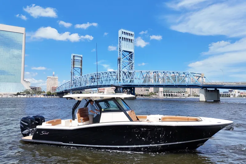 Slide: The Image of 2021 Scout 330 LXF boat cruising near a blue bridge under a clear sky. - 5