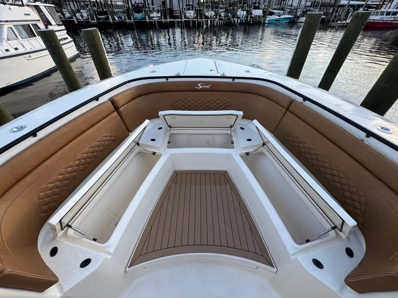 Slide: The Image of 2021 Scout 330 LXF boat interior with tan seating and storage compartments at a marina. - 53