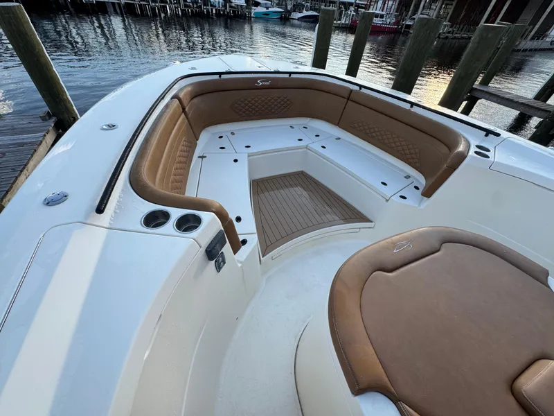 Slide: The Image of 2021 Scout 330 LXF boat interior with tan seating and wood accents at a dock. - 54