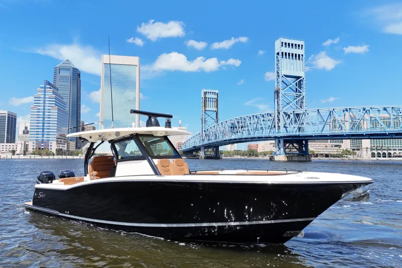 Slide: The Image of 2021 Scout 330 LXF boat on water with city skyline and bridge in background. - 6