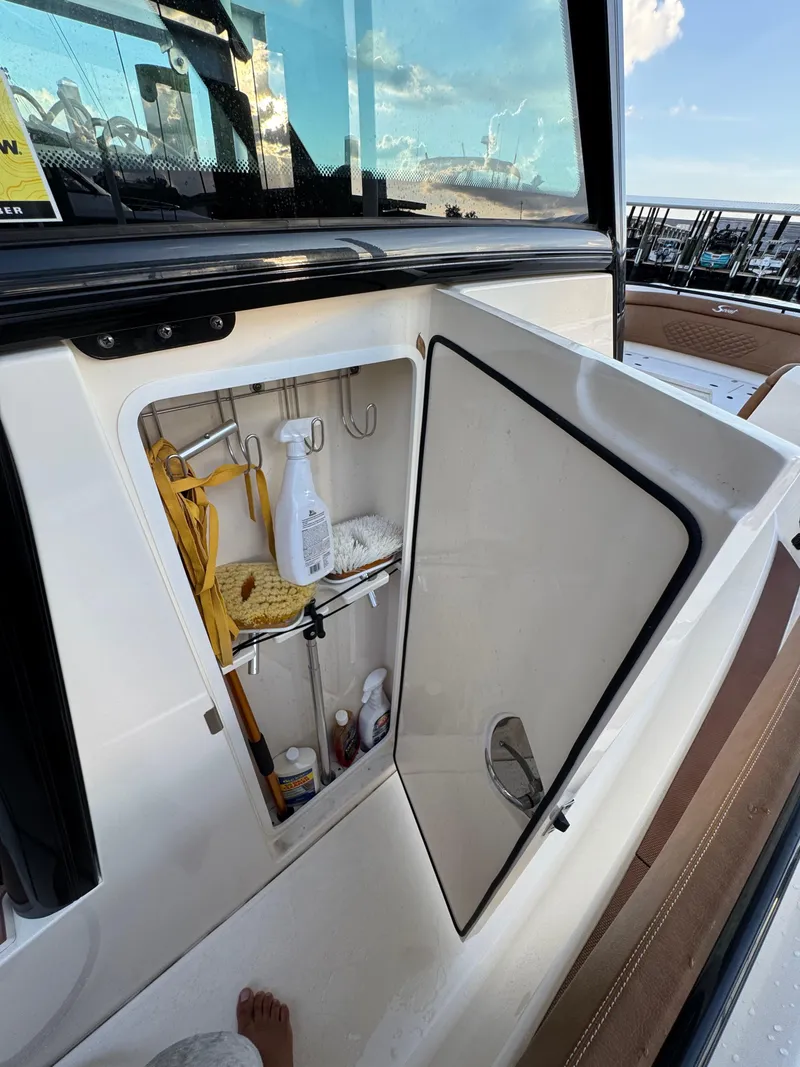 Slide: The Image of Open storage compartment on a 2021 Scout 330 LXF boat, containing cleaning supplies. - 69