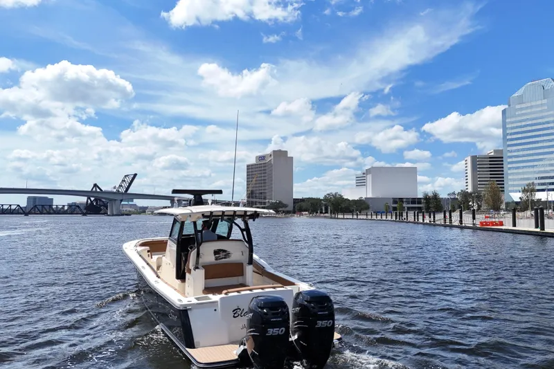 Slide: The Image of 2021 Scout 330 LXF boat cruising on a river with city skyline and bridge. - 89