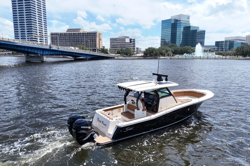 Slide: The Image of 2021 Scout 330 LXF boat cruising on urban river with cityscape background. - 90