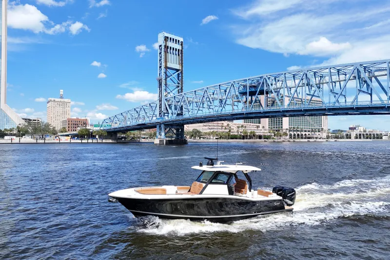 Slide: The Image of 2021 Scout 330 LXF boat cruising under a blue bridge on a sunny day. - 91