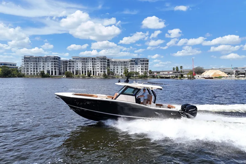 Slide: The Image of 2021 Scout 330 LXF boat cruising on a river with modern buildings in the background. - 99
