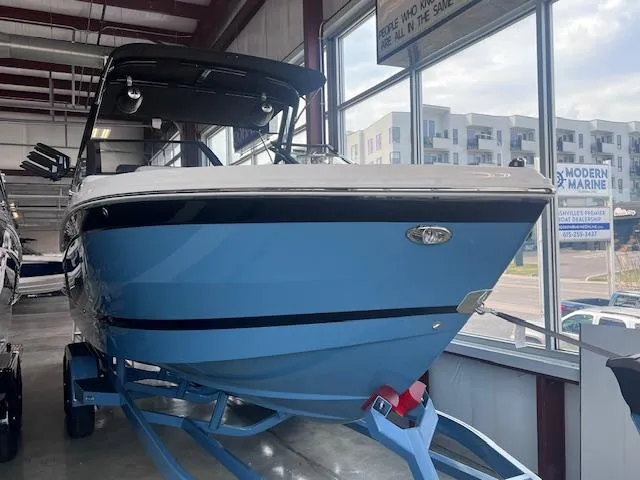 Slide: The Image of 2025 Cobalt R6 Surf boat in showroom, blue hull, on trailer, modern design. - 2