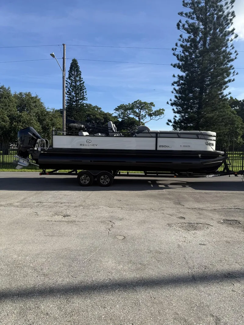 Slide: The Image of 2024 Regency 250 DL3 pontoon boat on trailer, parked outdoors. - 3