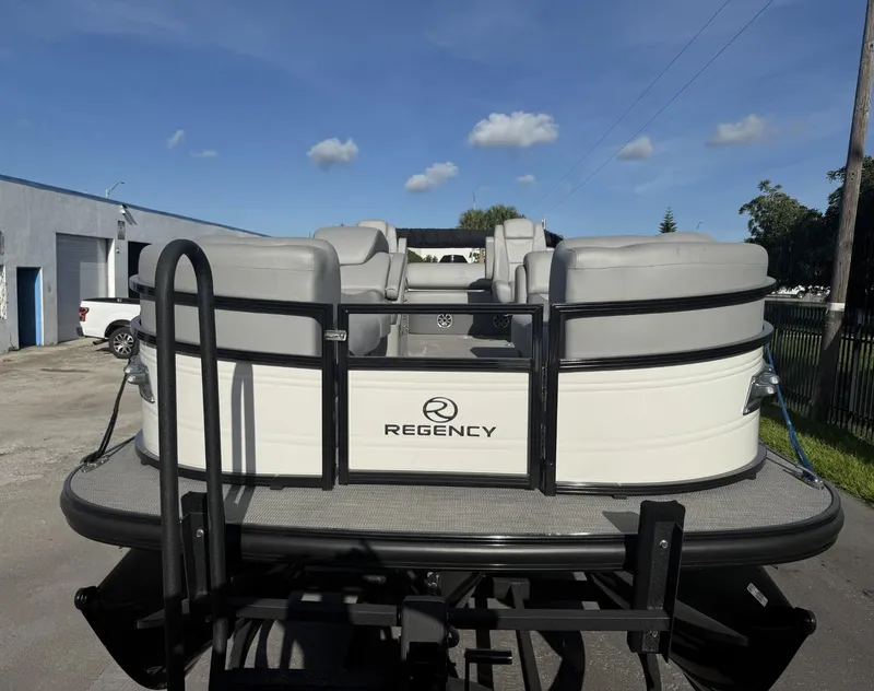 Slide: The Image of 2024 Regency 250 DL3 pontoon boat, rear view, parked outdoors under a clear blue sky. - 4