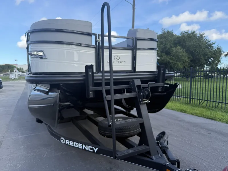 Slide: The Image of 2024 Regency 250 DL3 pontoon boat on trailer, parked outdoors under blue sky. - 5