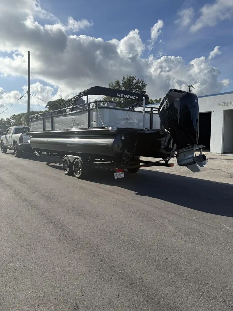 Slide: The Image of 2024 Regency 250 DL3 pontoon boat on trailer, parked on sunny street. - 6