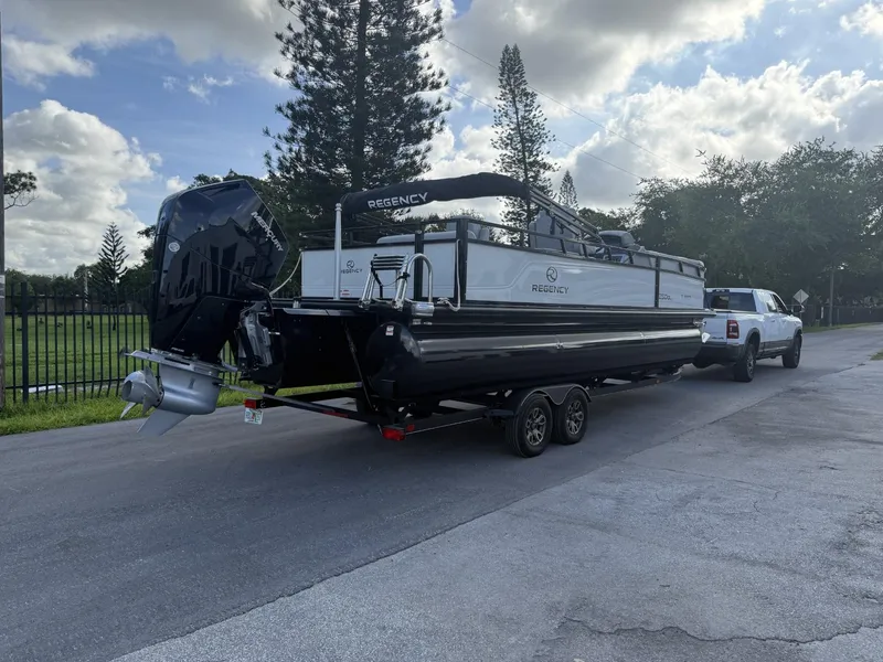 Slide: The Image of 2024 Regency 250 DL3 pontoon boat on trailer, parked on a sunny street. - 7