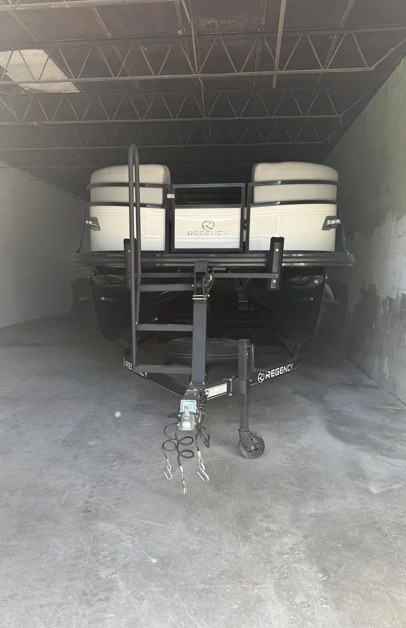 Slide: The Image of 2024 Regency 250 DL3 pontoon boat in storage, front view with trailer. - 8