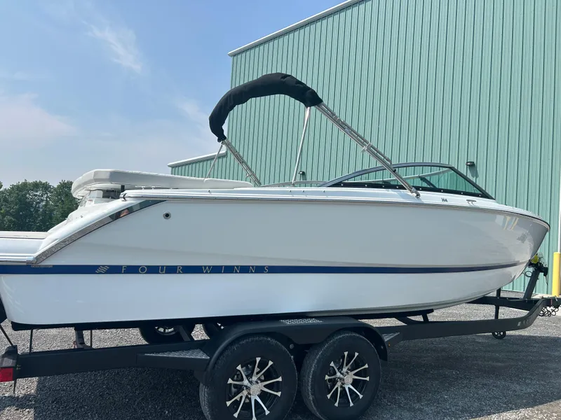 Slide: The Image of 2026 Four Winns H4 Freedom boat on trailer, parked near a green building. - 3