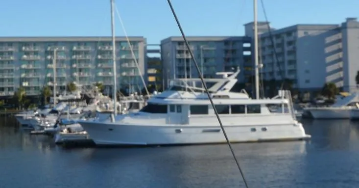 The Image of 1998 Hatteras 74 Sport Deck yacht docked in marina, with modern buildings in background. - 0