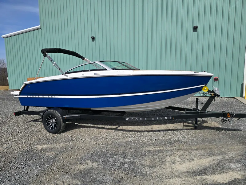 Slide: The Image of 2025 Four Winns H1 boat on trailer, blue hull, parked outdoors. - 1