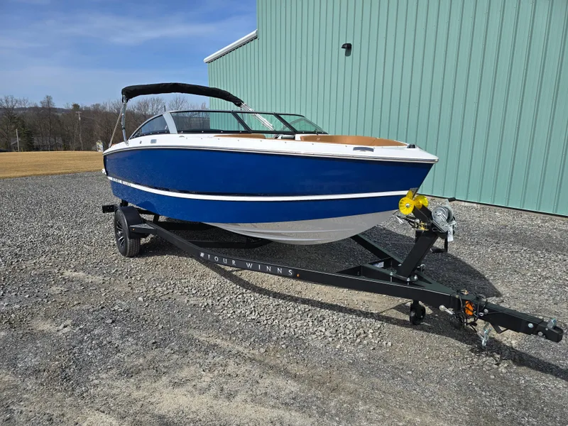 Slide: The Image of 2025 Four Winns H1 boat on trailer, blue and white, parked outdoors. - 2