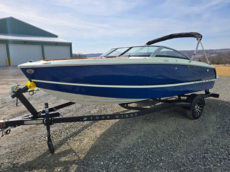 Slide: The Image of 2025 Four Winns H1 boat on trailer, blue hull, parked outdoors. - 9